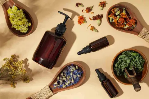 Botellas de vidrio ámbar con goteros y cucharas de madera con hierbas secas y flores, sugiriendo remedios naturales como flores de Bach para perros.