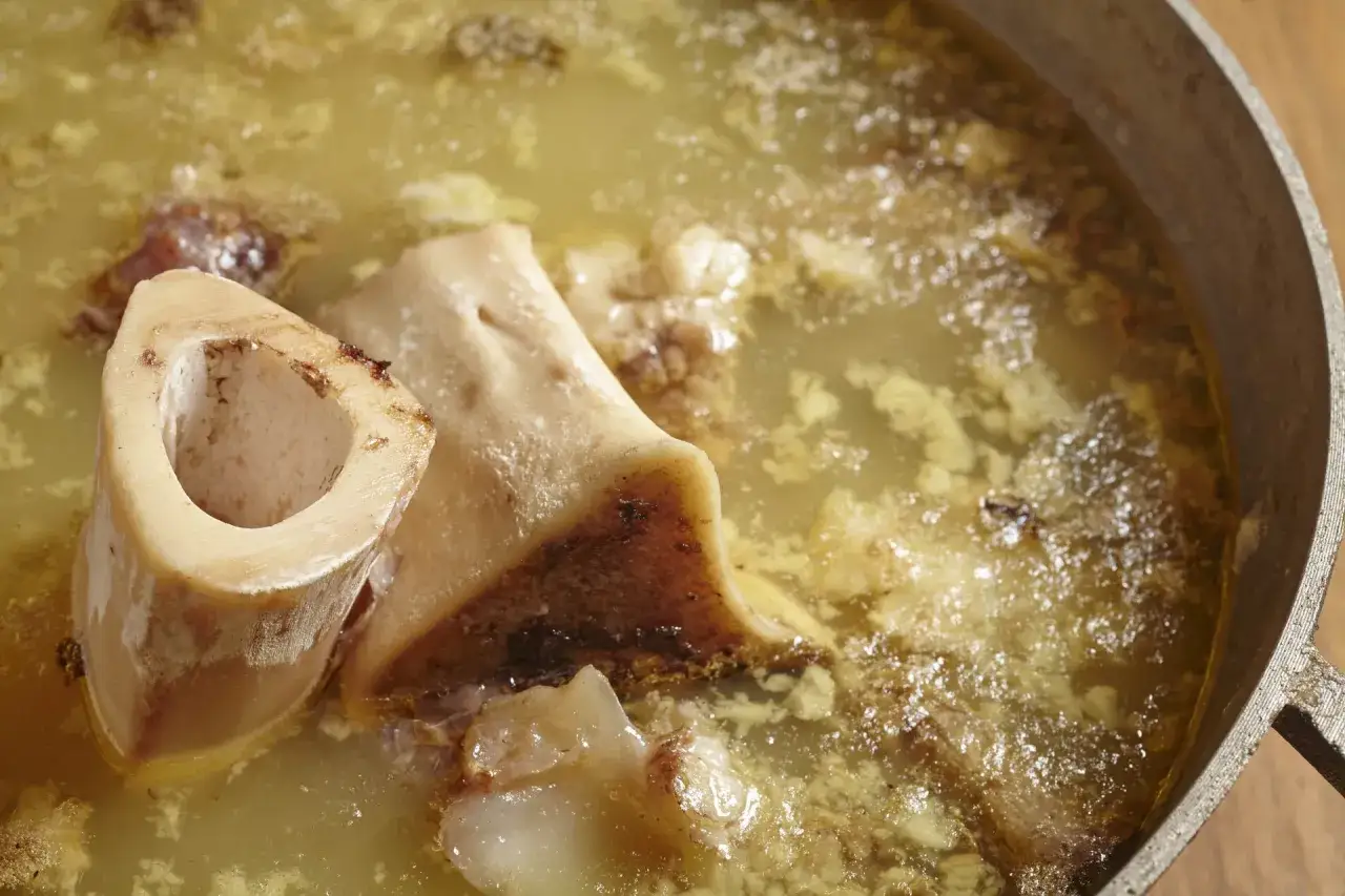 Un primer plano de un caldo de huesos para perros en una olla. Los huesos grandes y cortados están sumergidos en un líquido dorado y turbio.